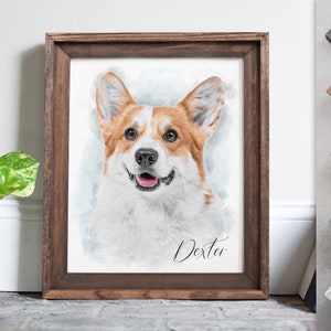 Op de afbeelding: Een aquarel van een corgi-hond met bruin en wit haar. De hond kijkt de kijker aan met een gelukkige uitdrukking. Het schilderij is ingelijst in een bruin houten lijst en heeft de naam "Dexter" in cursief onderaan.