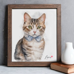 May include: A watercolor painting of a tabby cat wearing a blue bow tie. The cat is looking directly at the viewer. The painting is framed in a brown wood frame and has the name "Luna" written in cursive at the bottom with a small red heart.