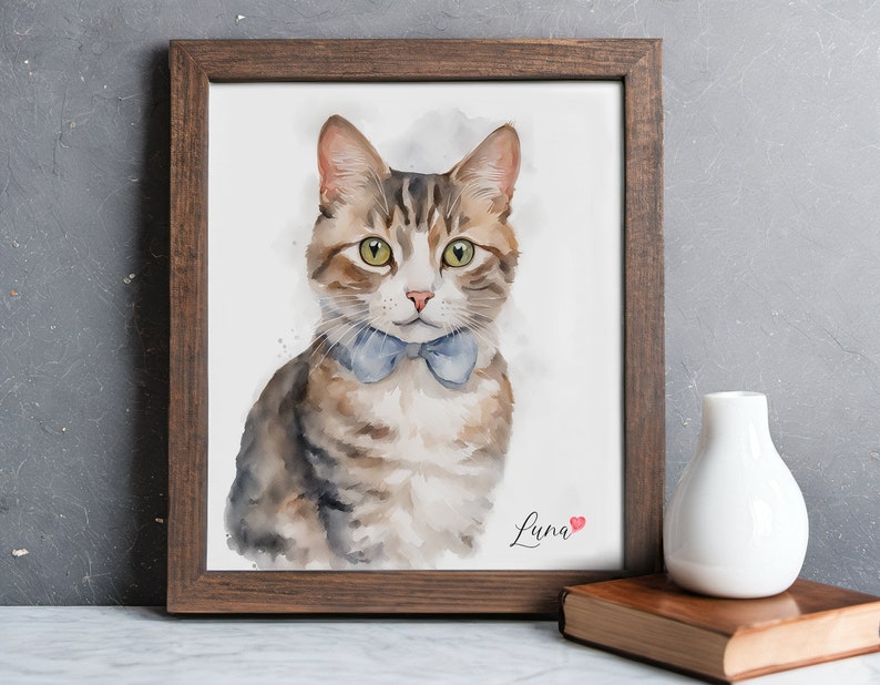 May include: A watercolor painting of a tabby cat wearing a blue bow tie. The cat is looking directly at the viewer. The painting is framed in a brown wood frame and has the name "Luna" written in cursive at the bottom with a small red heart.