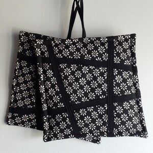 May include: Two black and white pot holders with a daisy print and black trim. The pot holders are hanging from a black string.