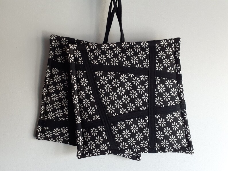 May include: Two black and white pot holders with a daisy print and black trim. The pot holders are hanging from a black string.