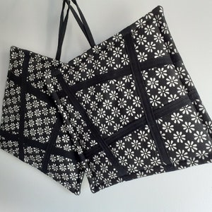 May include: Two black fabric tote bags with white daisy print. The bags have black straps and are made of a quilted fabric.