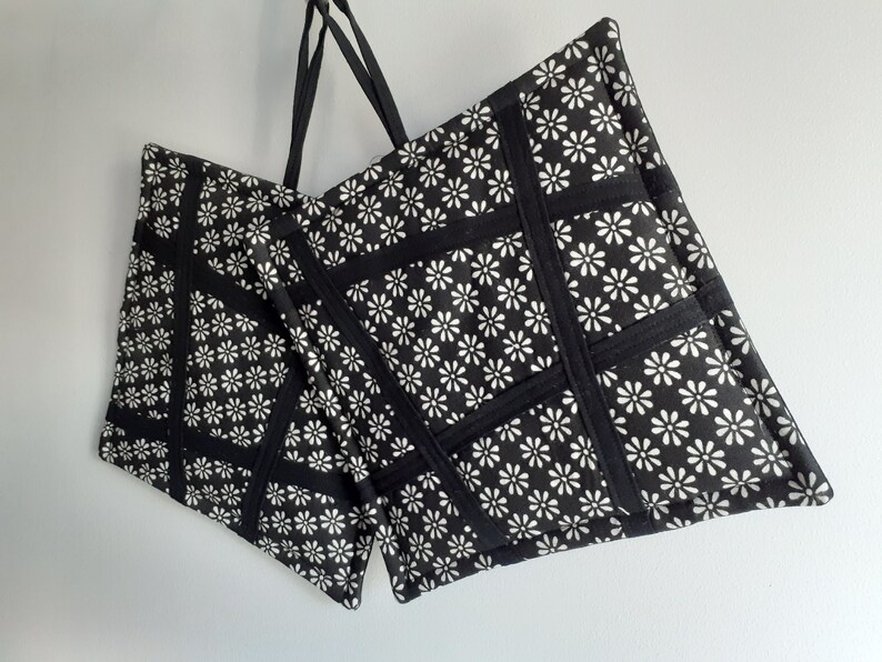 May include: Two black fabric tote bags with white daisy print. The bags have black straps and are made of a quilted fabric.