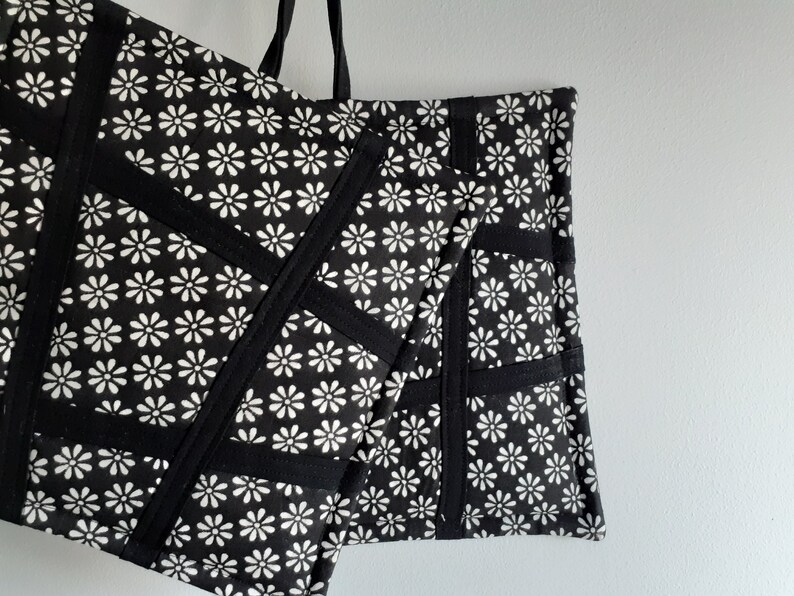 May include: Black and white tote bag with a daisy print and black fabric accents. The bag has a large capacity and is made of durable fabric.