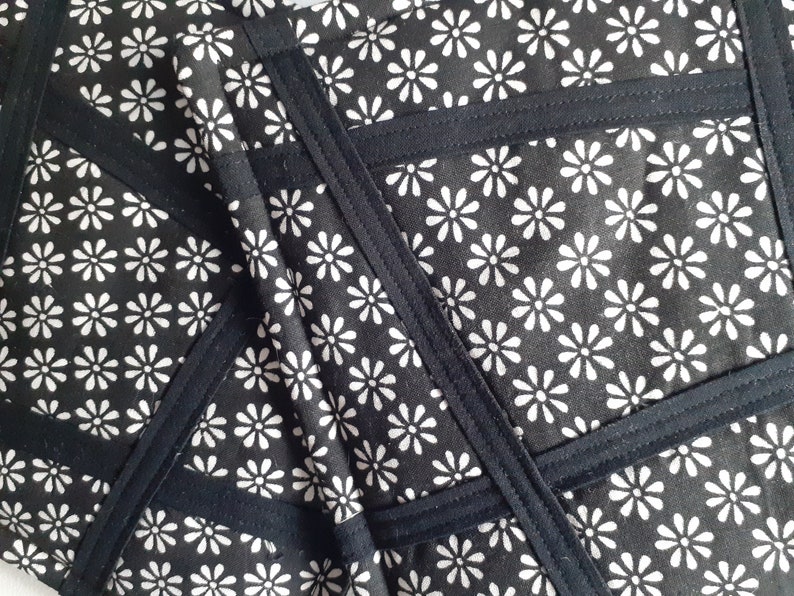 May include: Black fabric with a white daisy pattern. The fabric is sewn together in a geometric pattern with black seams.