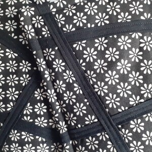 May include: Black fabric with a white daisy pattern. The fabric is sewn together in a geometric pattern with black seams.
