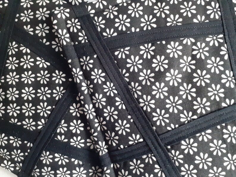 May include: Black fabric with a white daisy pattern. The fabric is sewn together in a geometric pattern with black seams.
