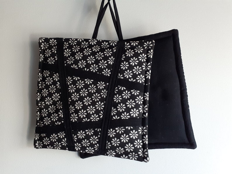 May include: Two black pot holders, one with a white floral pattern and the other plain. The pot holders are hanging from a white wall.
