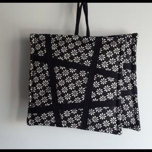 May include: Black tote bag with white daisy print and black straps. The bag is made of fabric and has a quilted design.