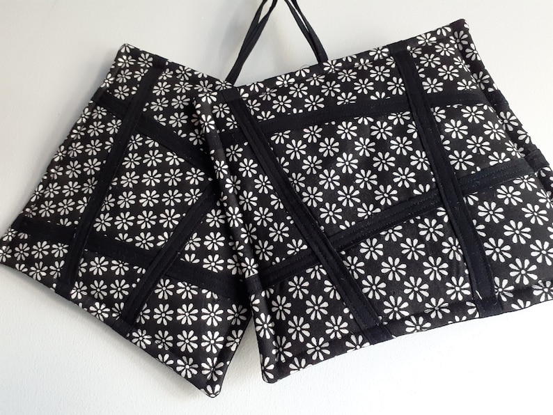 May include: Two black and white pot holders with a daisy print and black trim. The pot holders are made of fabric and have a quilted design.