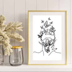 Op de afbeelding: Een ingelijste muurkunstprint met een zwarte lijntekening op een witte achtergrond. De illustratie toont het silhouet van een menselijk hoofd en hand, geïntegreerd met meerdere vlindervormen en bladvormige elementen in een doorlopende lijnstijl.