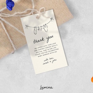 May include: A white thank you card with black text and a simple line drawing of baby clothes hanging on a clothesline. The text reads "thank you" and "We appreciate your love and support during such a special time in our life. Thank you for celebrating baby Marsha with us!" with love, Sarah & John. Lumina.