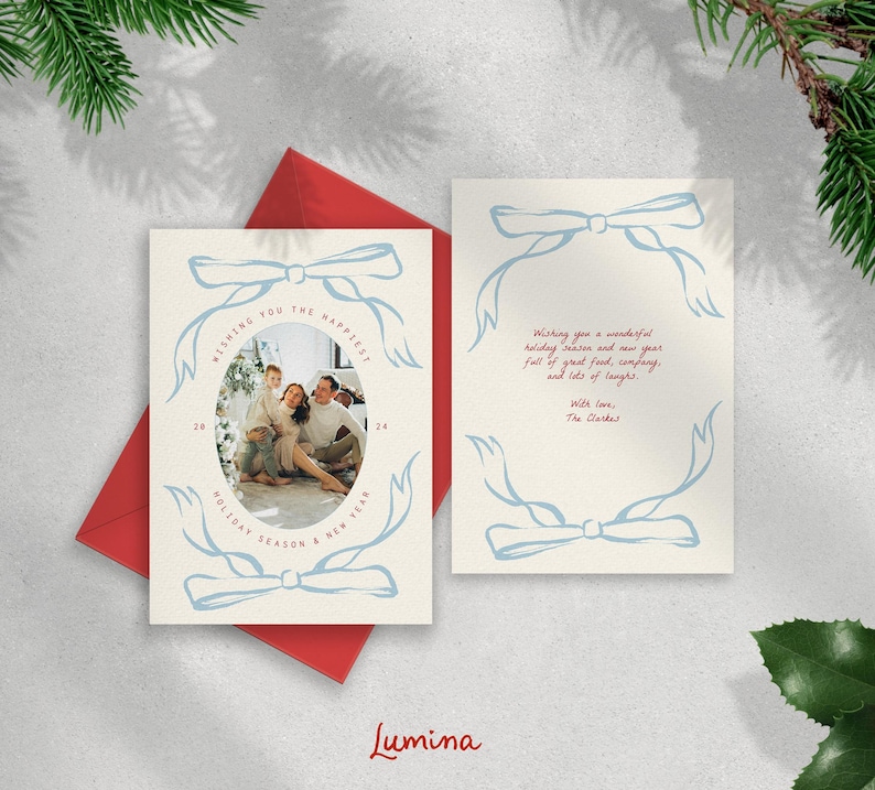 May include: A Christmas card with a blue and white illustration of a bow and a family photo inside. The text on the card reads "Wishing you the happiest holiday season & new year".