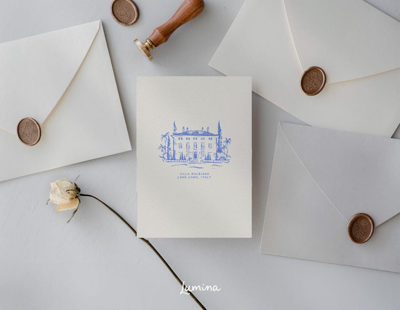 May include: A white card with a blue illustration of a building with trees and the text "Villa Balbiano, Lake Como, Italy". The card is surrounded by white envelopes with wax seals.