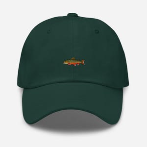 Pode incluir: Boné de beisebol verde escuro com um desenho de peixe bordado. O peixe é detalhado com tons de verde, laranja e vermelho. O boné tem uma viseira curva e uma alça ajustável na parte de trás.