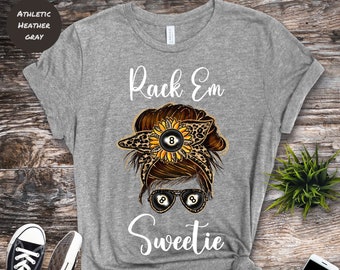 May include: A heather gray t-shirt with a graphic of a woman with a messy bun, sunglasses, and a sunflower with a black 8-ball in the center. The text "Rack Em Sweetie" is printed on the shirt.