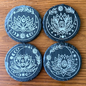 May include: Set of four black slate coasters with a white design of a lotus flower, moon, and stars.