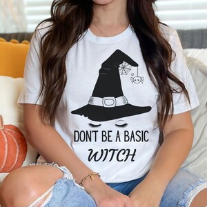 May include: White t-shirt with a black witch hat and spider graphic. The text "Don't be a basic witch" is printed on the shirt.