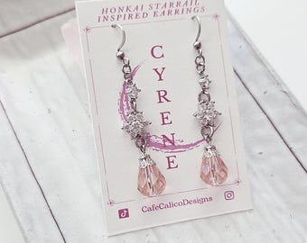 May include: Silver-toned earrings with clear and pink accents. The earrings feature a series of clear crystals and pink teardrop-shaped beads. The card behind the earrings reads "HONKAI STARRAIL INSPIRED EARRINGS" and "CYRENE" with a social media handle.