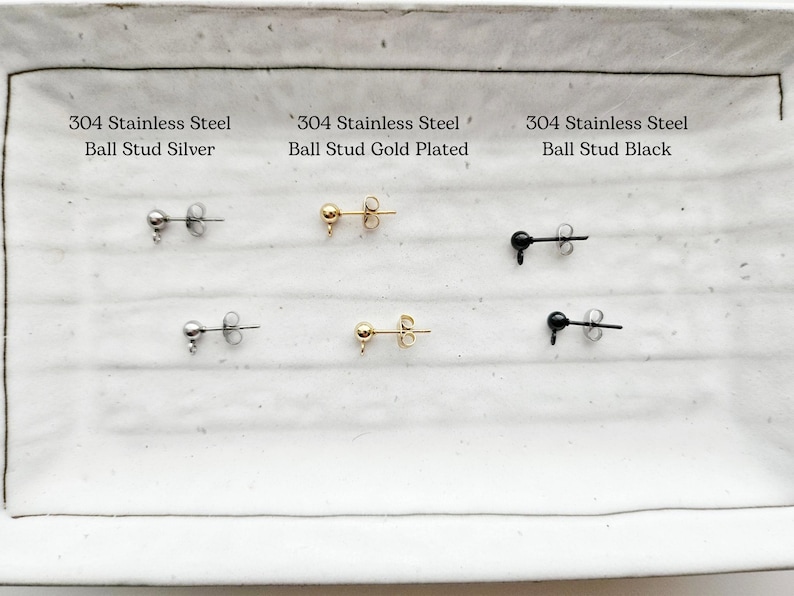 May include: A selection of ball stud earrings in silver, gold-plated, and black. Each pair is made of 304 stainless steel. The earrings are displayed on a white rectangular surface with text labels.