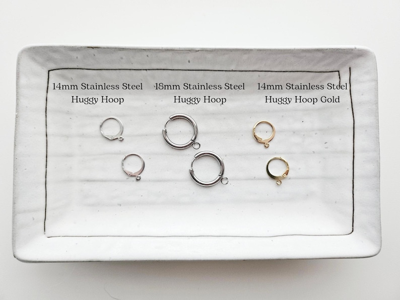 K&ouml;nnte beinhalten: Vier Paar Huggie-Creolen auf einem wei&szlig;en Keramikteller. Die Ohrringe sind aus Edelstahl und in Silber und Gold erh&auml;ltlich. Der Text auf dem Teller lautet: "14mm Stainless Steel Huggy Hoop", "18mm Stainless Steel Huggy Hoop" und "14mm Stainless Steel Huggy Hoop Gold".