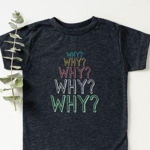 Op de afbeelding: Een donkergrijs T-shirt met het woord "WHY?" vijf keer herhaald in verschillende kleuren, waaronder turquoise, roze, geel en groen.