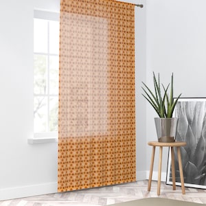 Può includere: Un pannello per tenda trasparente caratterizzato da un motivo ripetuto di piccole forme a goccia color arancione scuro su uno sfondo arancione più chiaro. Il tessuto è traslucido, lasciando passare la luce e mettendo in risalto la stampa.