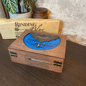 May include: A wooden box with a blue and white starry sky design on the lid. The lid is open and the inside of the box is visible. The box is engraved with the words "you do not yield".