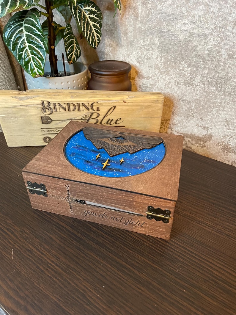 May include: A wooden box with a blue and white starry sky design on the lid. The lid is open and the inside of the box is visible. The box is engraved with the words "you do not yield".