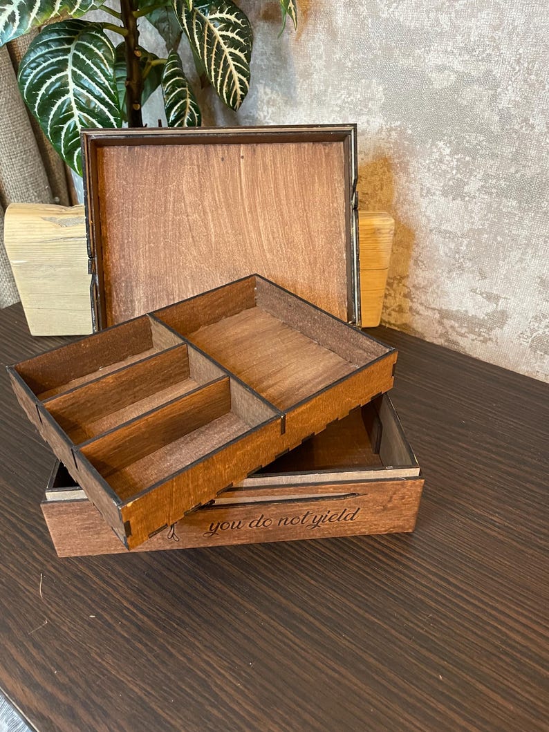 May include: A wooden box with a hinged lid and a removable tray. The tray has four compartments. The box is engraved with the text "you do not yield".