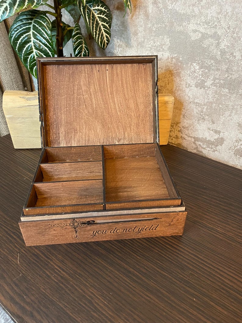 May include: A wooden box with a hinged lid and a divided interior. The box is engraved with the words "you do not yield".