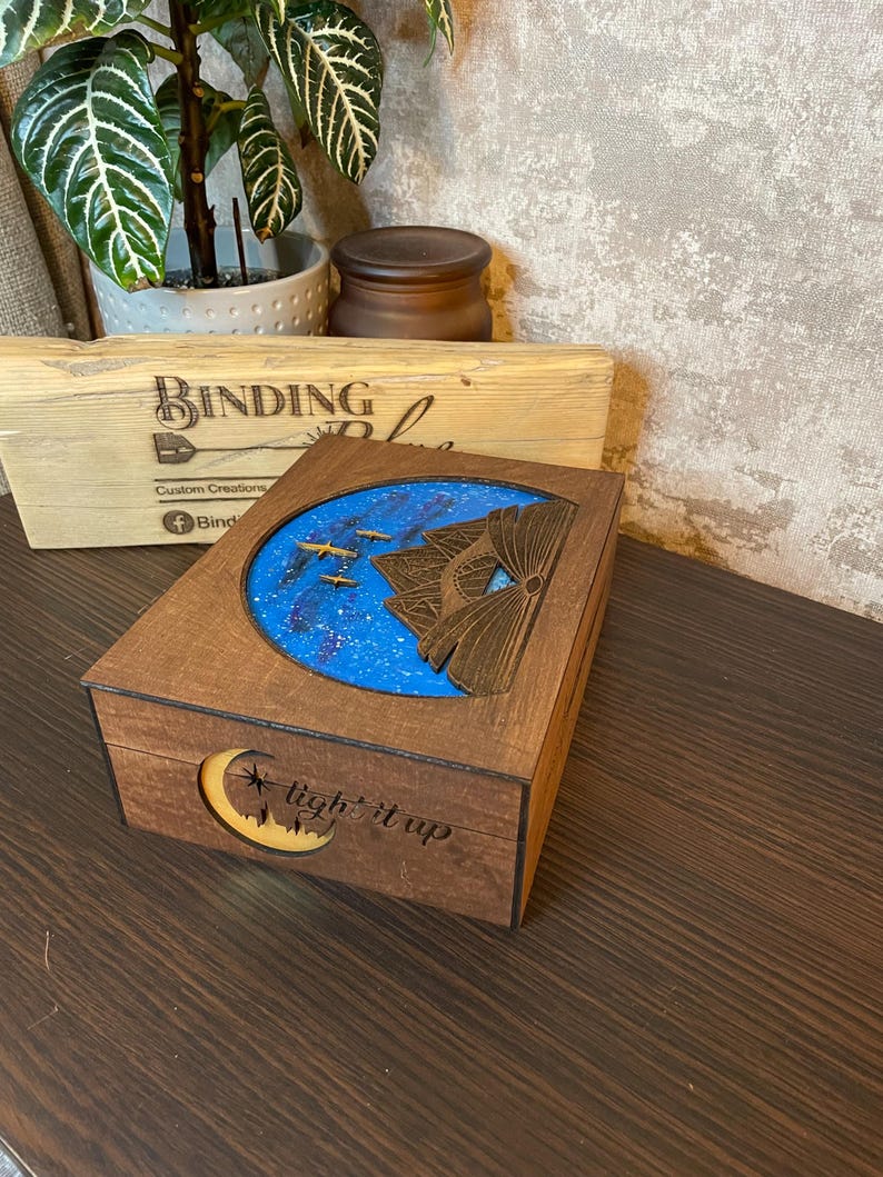 May include: A wooden box with a blue and white starry sky scene inside. The box has a crescent moon with the words "light it up" carved into the wood.