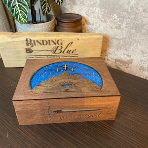 May include: A wooden box with a blue and gold mountain scene on the lid. The box is engraved with the words "you do not yield".