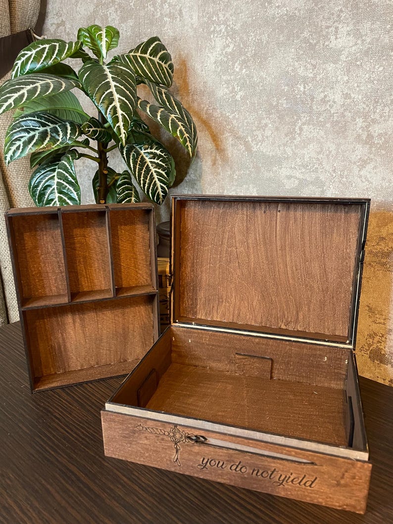 May include: A wooden box with a drawer and a removable top section. The box has a compartment with multiple sections. The drawer has a rope design and the text "you do not yield" engraved on it.