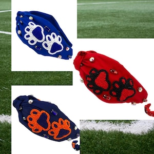 Op de afbeelding: Drie hoofdbanden met poot afdruk ontwerpen. De hoofdbanden zijn blauw, rood en donkerblauw. Elke hoofdband heeft een ander gekleurd poot afdruk ontwerp. De poot afdrukken zijn gemaakt van kralen en strass.