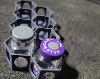 May include: A gray hexagonal storage container with two clear glass bottles. One bottle has a purple lid with the text "Allergan 100UL" printed on it. The other bottle has a gray lid.