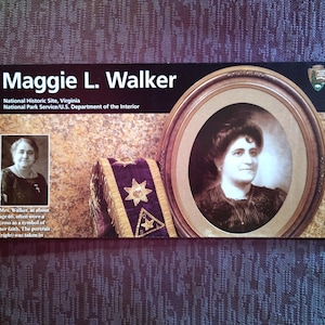 May include: A black and white portrait of Maggie L. Walker, a prominent African American businesswoman and activist, at the Maggie L. Walker National Historic Site in Richmond, Virginia. The portrait shows her wearing a dark dress and a cross around her neck. The text "Mrs. Walker, at about age 60, often wore a cross as a symbol of her faith. The portrait (right) was taken in..." is visible at the bottom of the image.