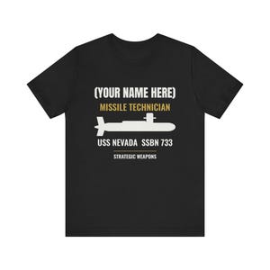 May include: A black short-sleeve t-shirt featuring a white silhouette of a submarine. The text reads (YOUR NAME HERE), MISSILE TECHNICIAN, USS NEVADA SSBN 733, and STRATEGIC WEAPONS in white and gold lettering centered on the chest area.