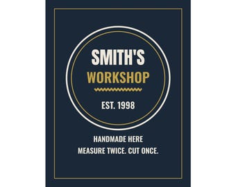 Puede incluir: Un letrero rectangular de color azul oscuro con un círculo central blanco con bordes dorados y blancos. El texto dice SMITH'S WORKSHOP, EST. 1998, HANDMADE HERE y MEASURE TWICE. CUT ONCE. El diseño incluye una línea dorada en zigzag y un borde fino.