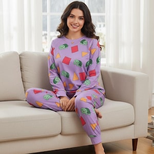 May include: A lilac pajama set featuring a repeating pattern of green cartoon turtles, red squares, and orange triangles. The long-sleeved top and matching pants are made of a soft material. The pajama set is designed for comfort and relaxation.