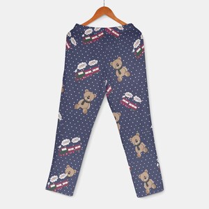 Op de afbeelding: Marineblauwe pyjamabroek met een herhaald patroon van teddyberen met groene sjaals en rode en groene treinen met het woord "choo" in witte tekstballonnen. De achtergrond is bedekt met kleine witte stippen.