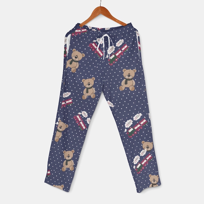 Op de afbeelding: Marineblauwe pyjamabroek met een herhalend patroon van teddyberen met sjaals en rode dubbeldekkerbussen. De broek heeft ook witte stippen en een taille met trekkoord.