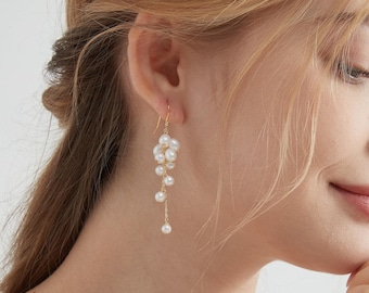 Puede incluir: Un par de pendientes largos y colgantes con un racimo de perlas blancas. Los pendientes están hechos de oro y tienen un delicado diseño de cadena.