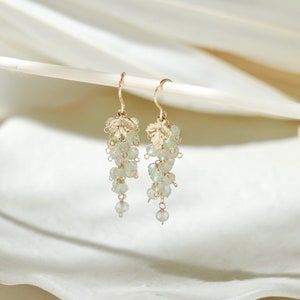 May include: Gold earrings with a leaf design and light green gemstone beads hanging from the bottom.