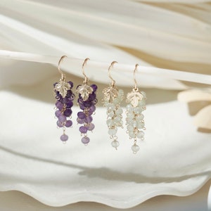 Op de afbeelding: Een paar gouden oorbellen met een druiventrosontwerp. De oorbellen hebben een waterval van amethist- en aquamarijn edelstenen.