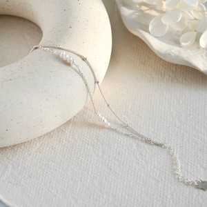 May include: A delicate silver chain bracelet with small white pearls. The bracelet has two chains, one with a delicate chain and the other with a slightly thicker chain.