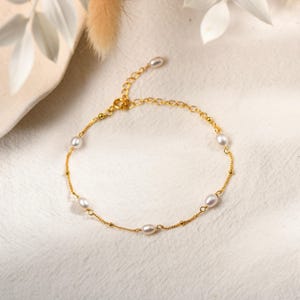 May include: A delicate gold bracelet featuring several small, oval-shaped pearls. The bracelet has a fine chain with small gold beads interspersed along its length. The clasp and connecting elements are also gold, creating a cohesive and elegant piece of jewelry.