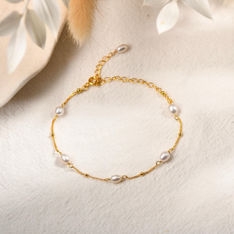 May include: A delicate gold bracelet featuring several small, oval-shaped pearls. The bracelet has a fine chain with small gold beads interspersed along its length. The clasp and connecting elements are also gold, creating a cohesive and elegant piece of jewelry.