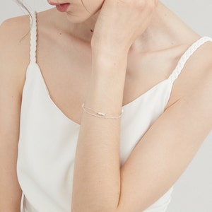 May include: A delicate silver chain bracelet with a row of small white pearls. The bracelet is layered with a thinner silver chain.