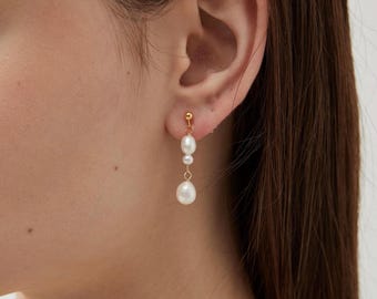 Puede incluir: Pendientes colgantes dorados con tres perlas blancas. Los pendientes tienen un pequeño perno dorado en la parte superior, con las perlas suspendidas debajo en delicadas cadenas doradas. Las perlas varían en tamaño, siendo la más grande la inferior.